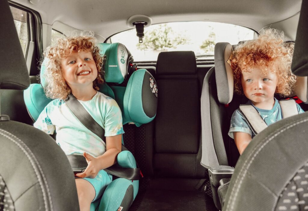 Two children sitting in car seats in the back seat of a car