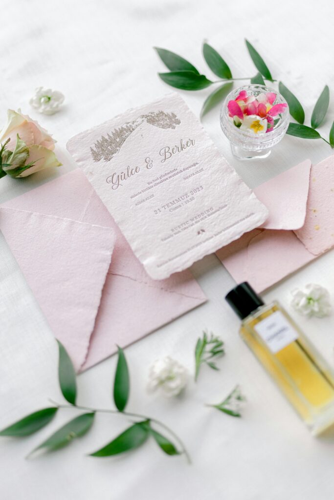 Pretty pink wedding invitation laid out on a table with flowers and perfume