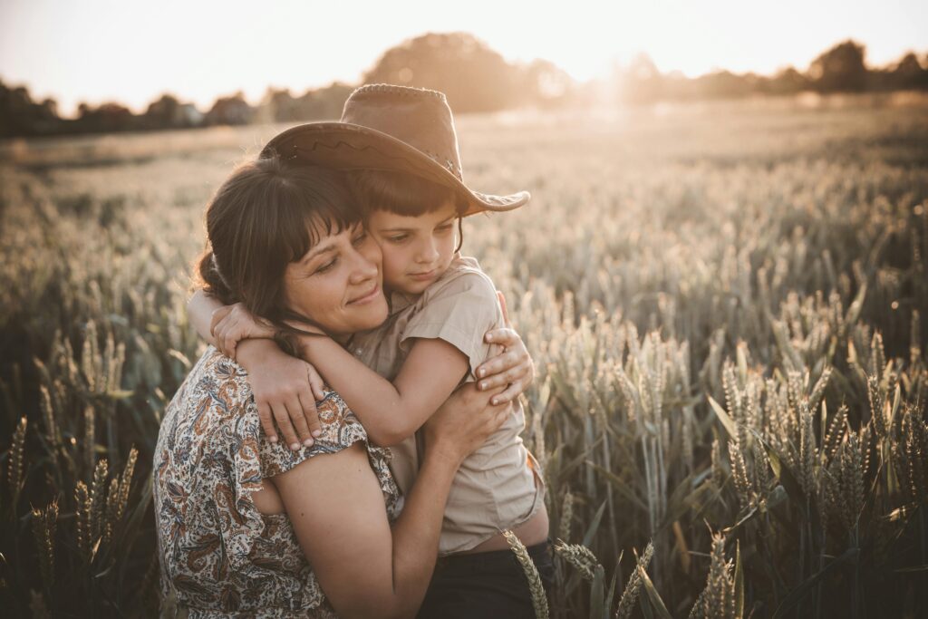Mother hugging child in a field with the sun behind them