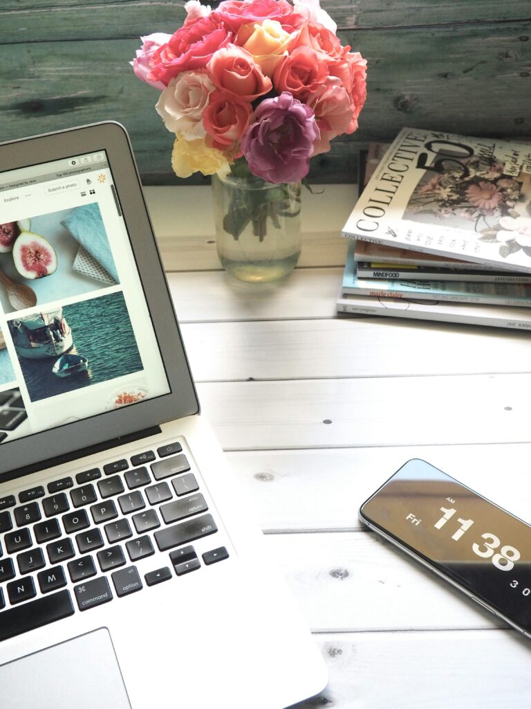 Desk laid out with a laptop. phone, flowers and fashion magazines