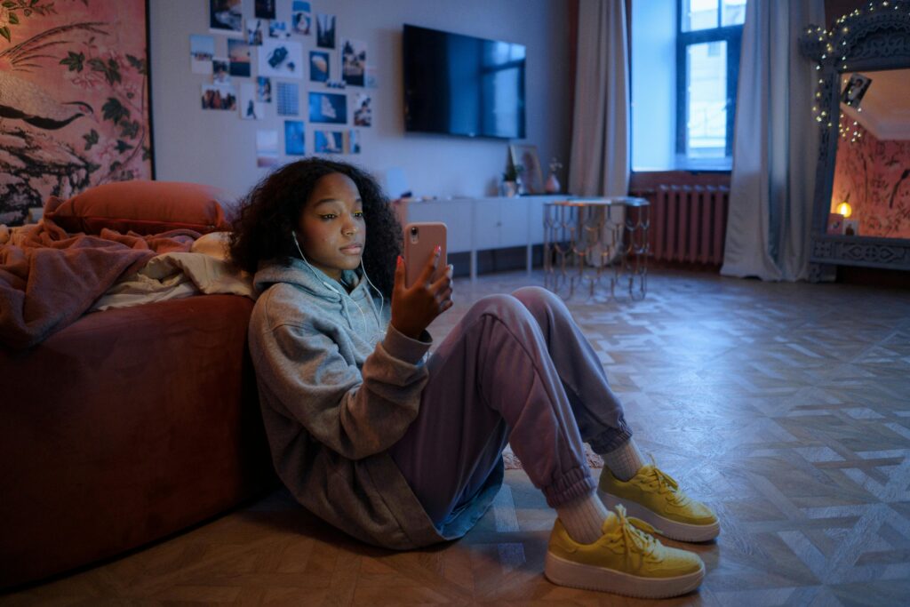 Pre-teen girl sitting on the floor of a living room looking at her phone in her hand