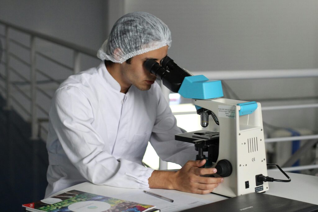 Image of man in white scrubs and a hairnet looking into a medical telescope