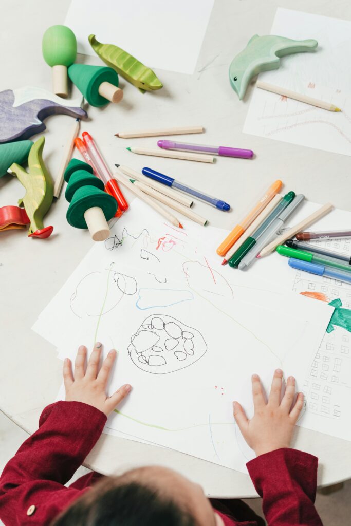 Child drawing surrounded by markers and toys