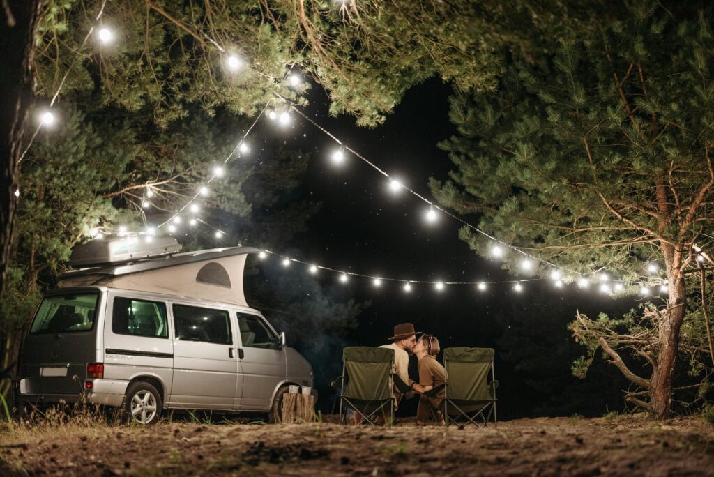 A couple kissing outside a campervan with string lights at night time