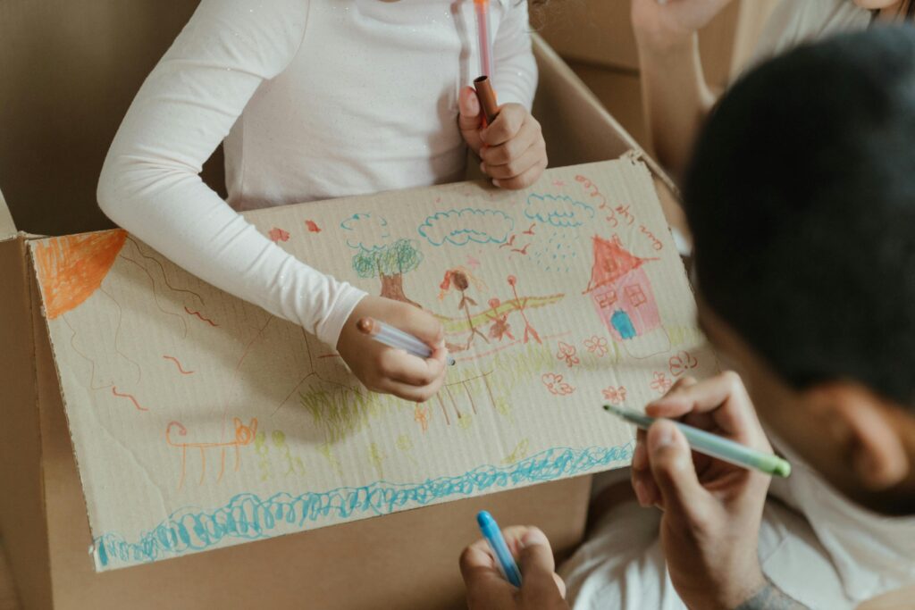 Child and parent drawing pictures on a cardboard box