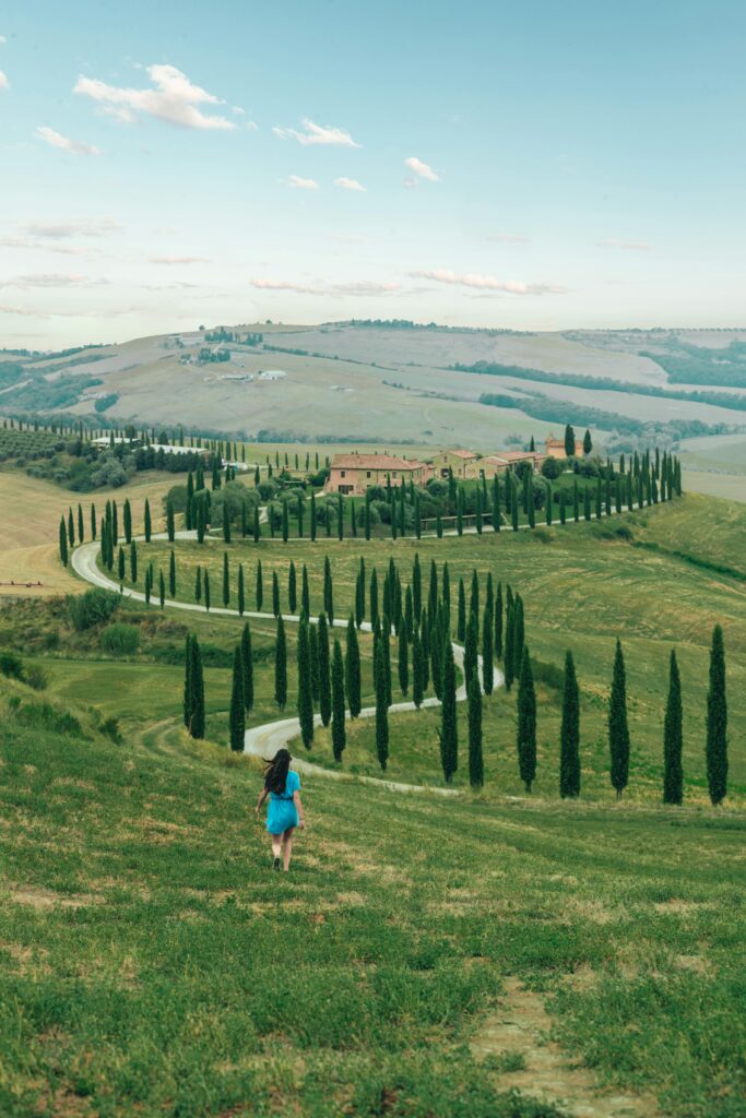 Woman walking through rolling green hills in Tuscany, Italy