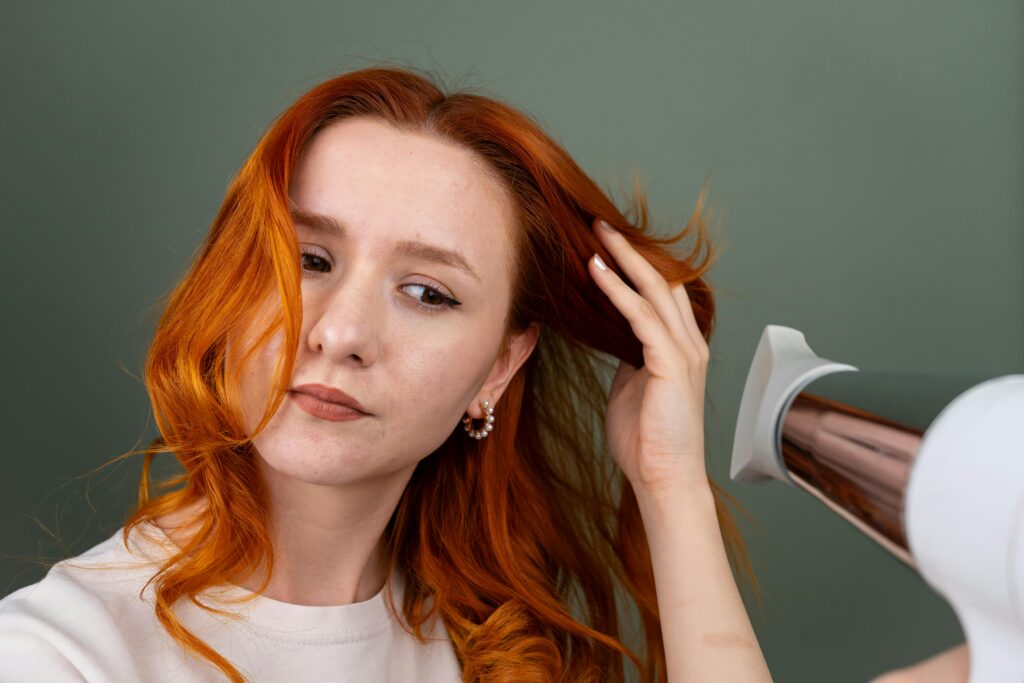 Young woman blow-drying red hair