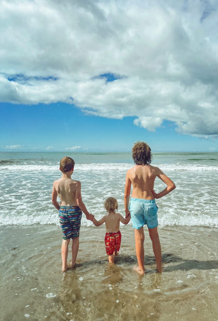 Three boys holding hands and facing the sea on a beach