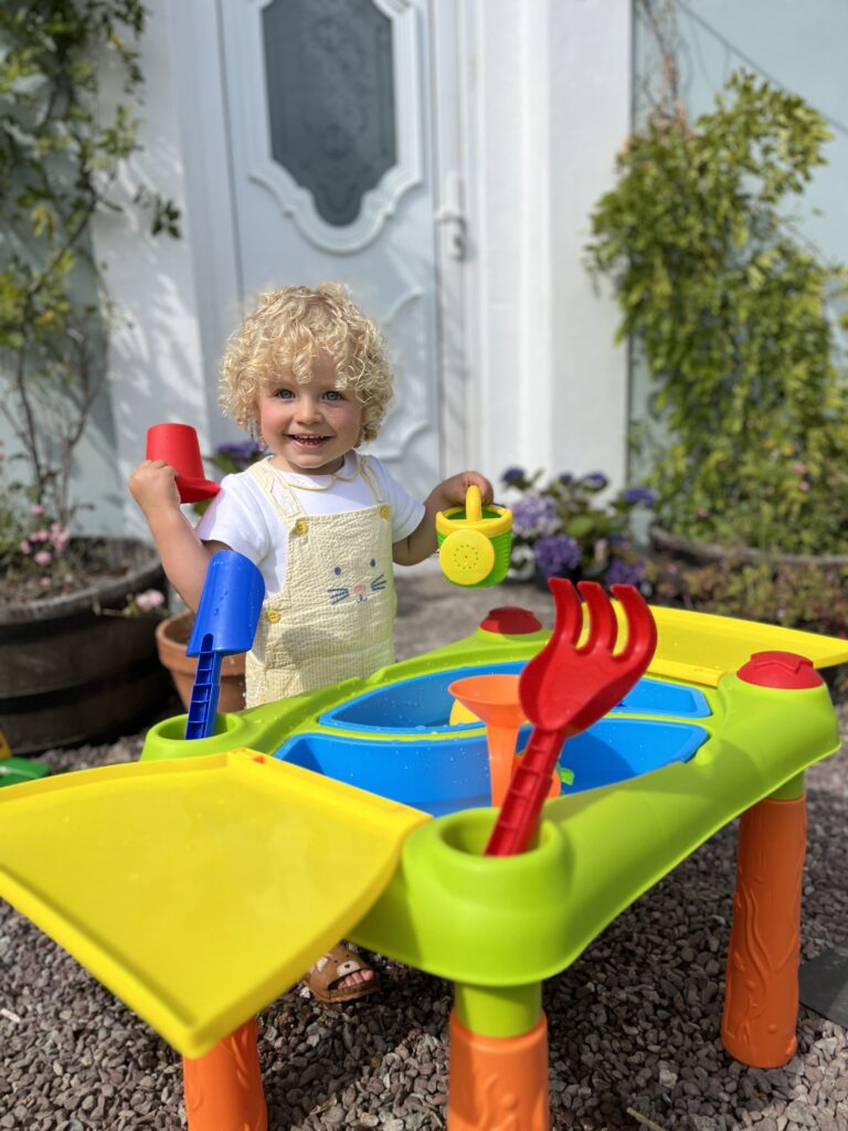 Curly haired boy playing with a sand and water table