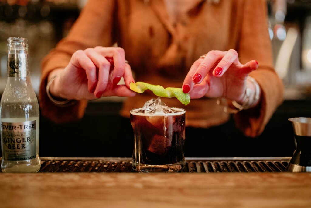 Woman holding a pickle over an alcoholic drink