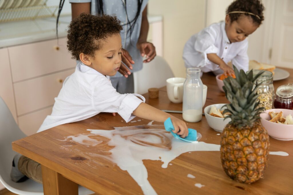 Young boy wiping up spilt milk from a table top