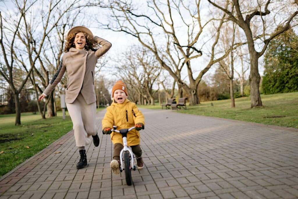Happy boy riding bicycle in autumn with his mother running beside him