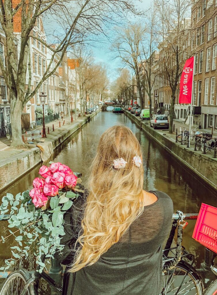 Woman with long hair standing by a canal in Amsterdam with a bouquet of pink roses