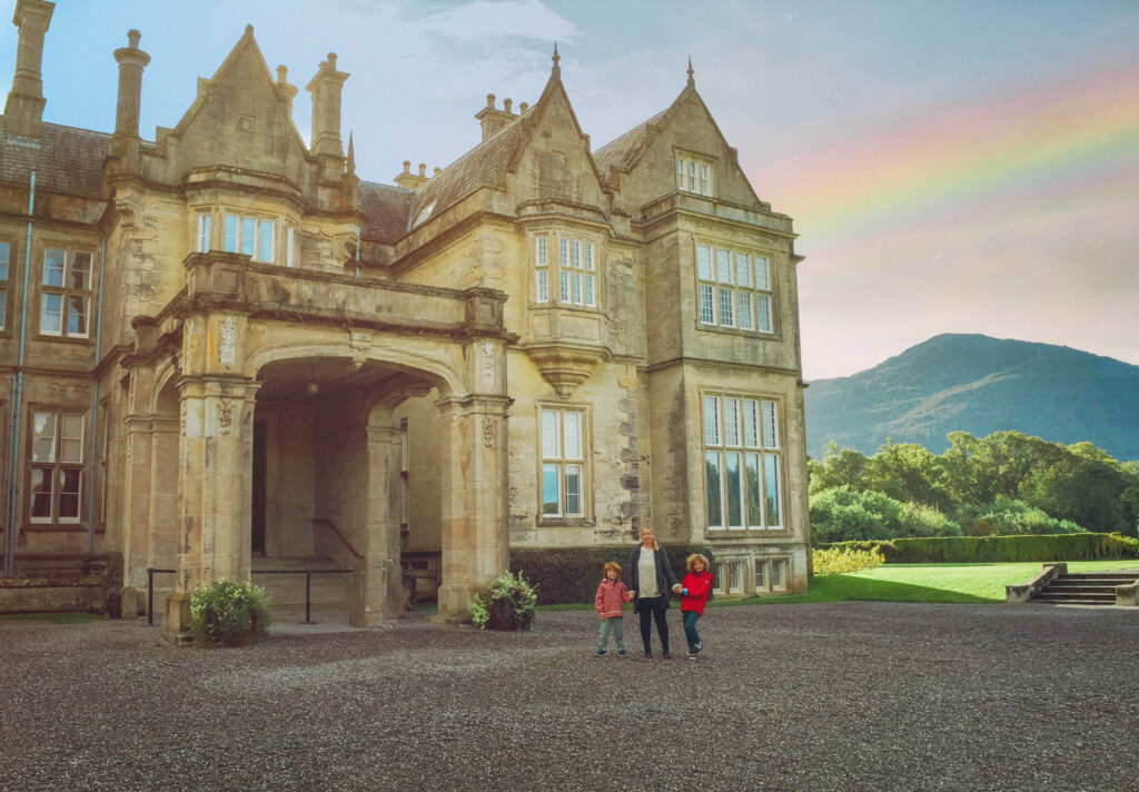 Woman and two children standing outside Muckross House with a rainbow in the sky
