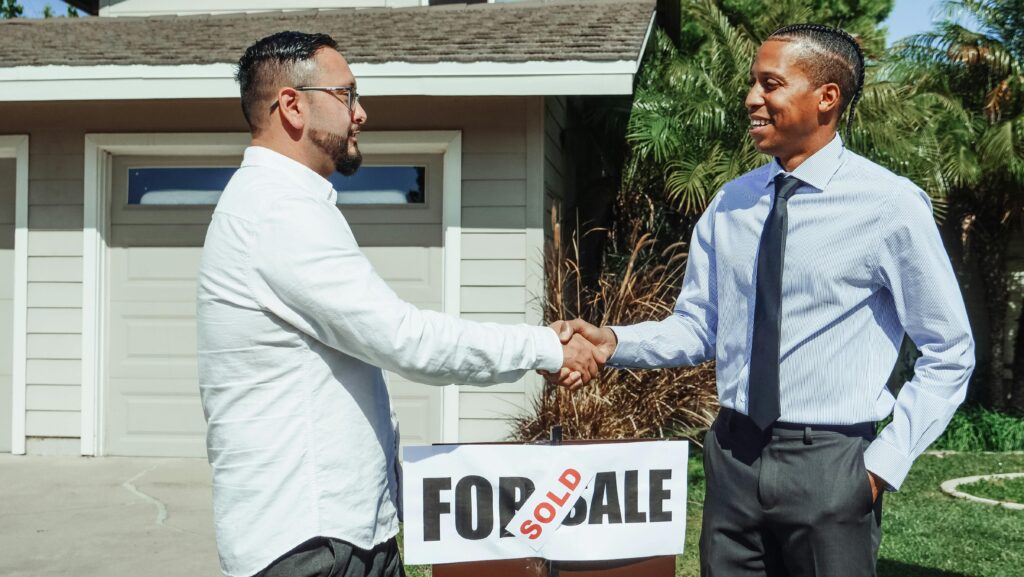 Two men shaking hands above a sale agreed sign