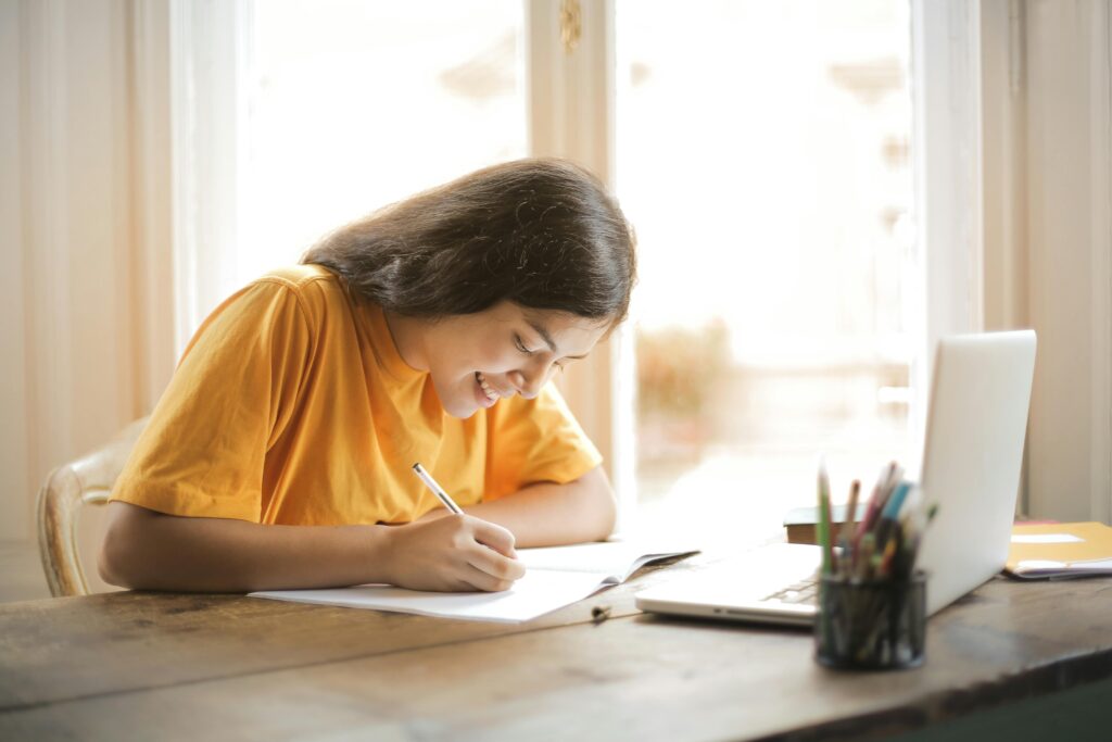Female in yellow shirt smiling while writing at a desk