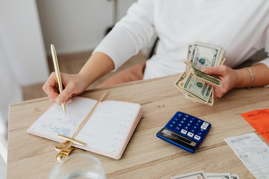 Unknown person writing in a diary and budgeting money with a calculator