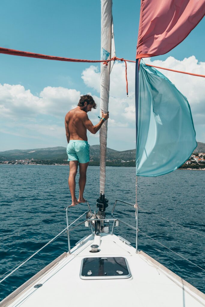 Man standing at the front of a sail boat in blue swimming shorts