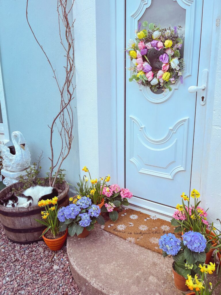 Floral wreath on a white door with colourful flowers in pots