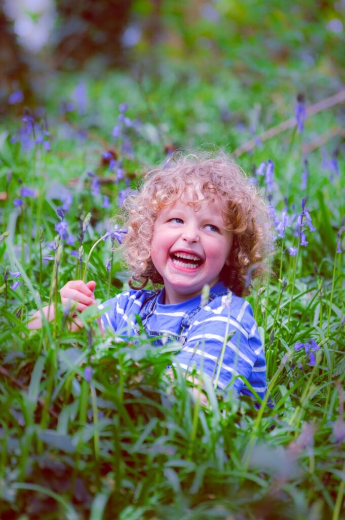 Blonde haired child laughing surrounded by bluebells