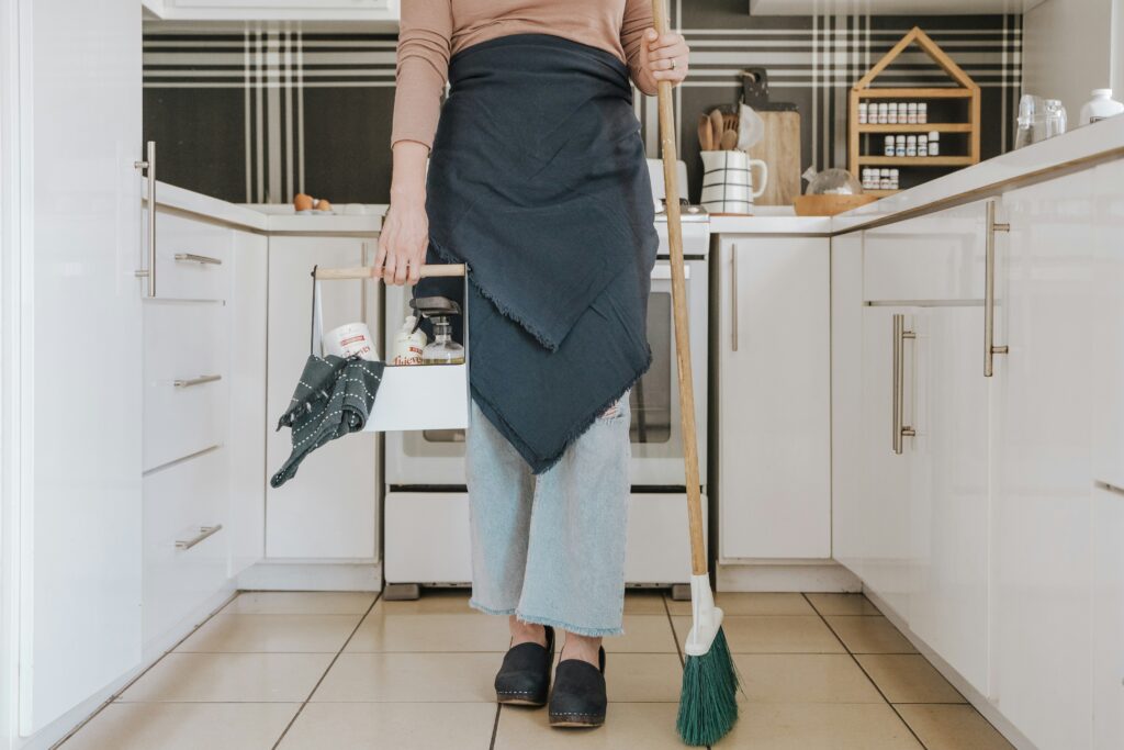 Anon person standing in a kitchen with cleaning supplies