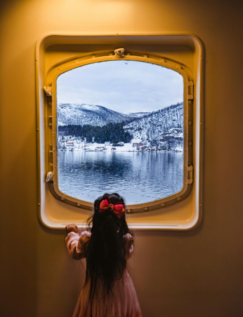 Little girl looking through a ship's window onto a snowy landscape