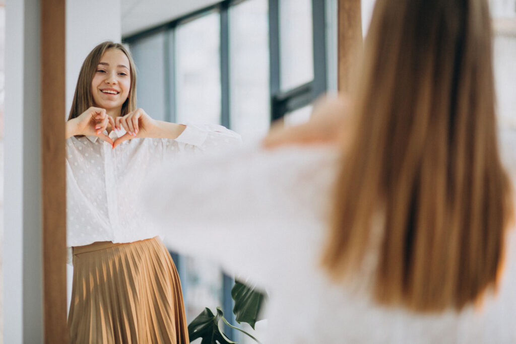 Pretty woman making a heart shape with her hands to a mirror