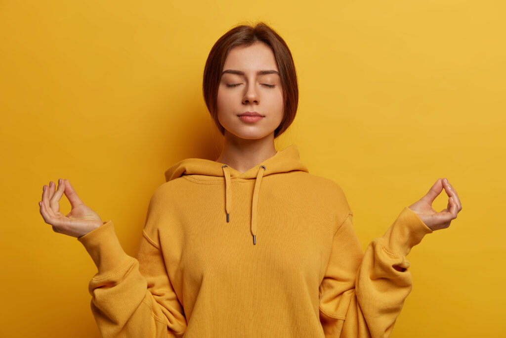 Girl meditating in yellow hoodie with yellow background