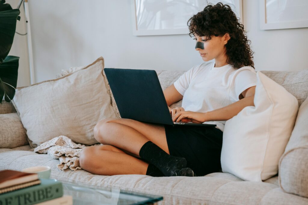 Woman sitting on a couch with a laptop while recovering from nose surgery
