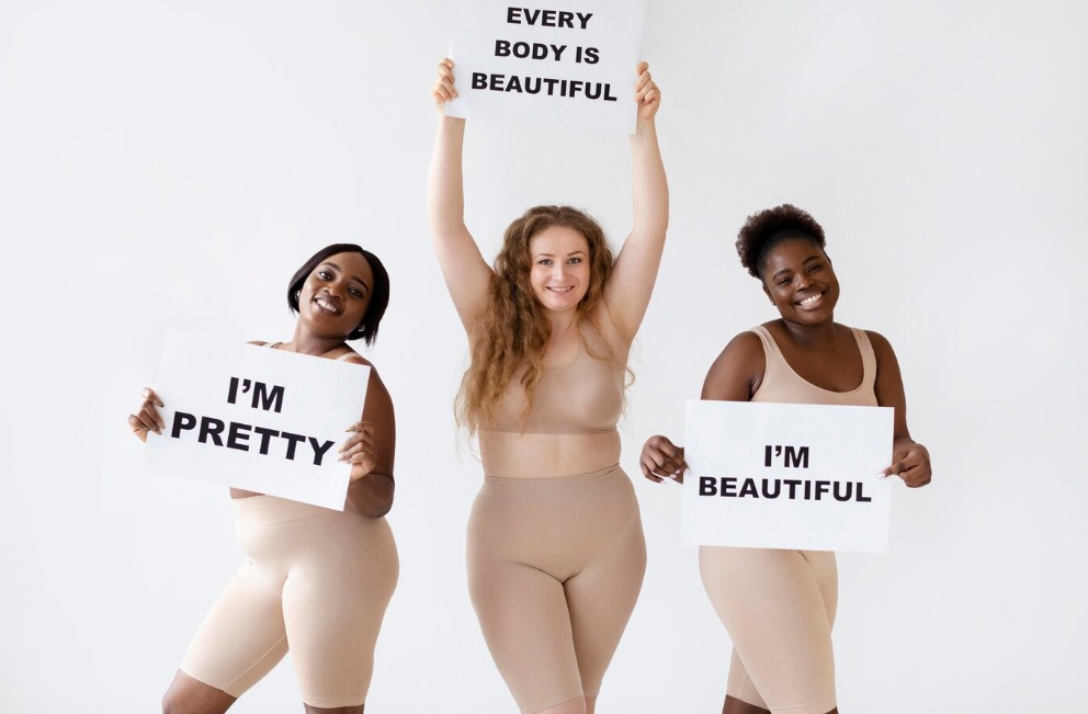 Three women holding body positivity slogans