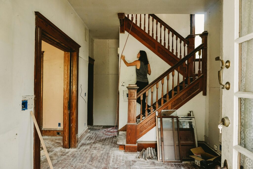 Woman in a grey tank top standing on the stairs of a fixer upper old house