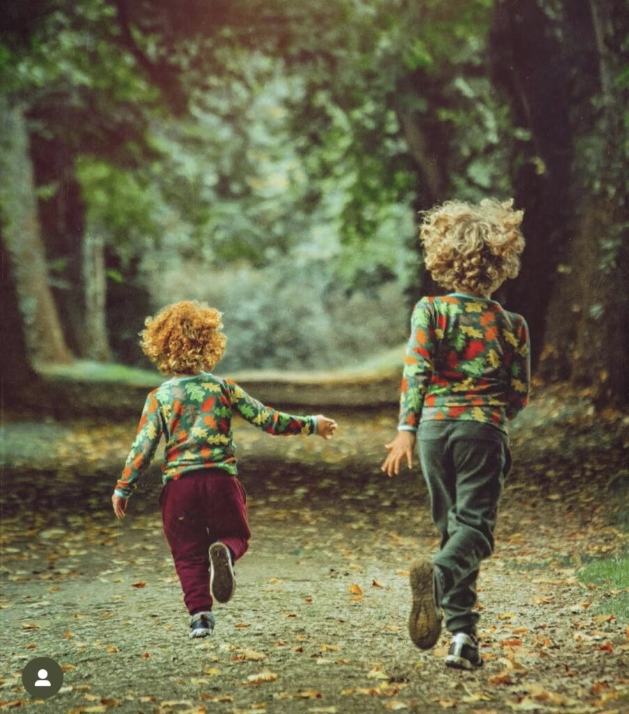 Two boys in leaf print shirts running on a leafy path