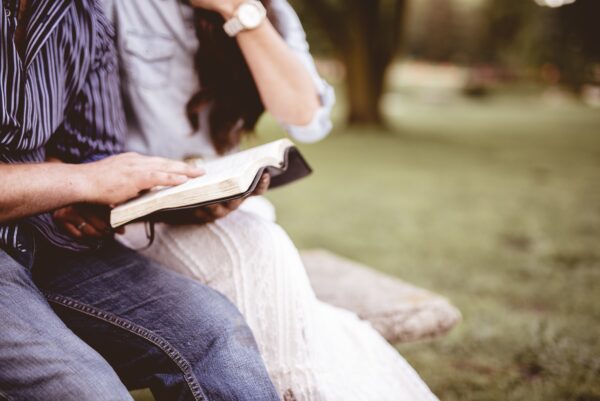 Anon couple sitting in a park reading the Bible
