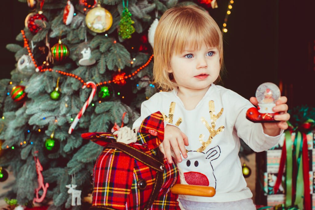 Little girl sitting on a hobby horse by Christmas tree