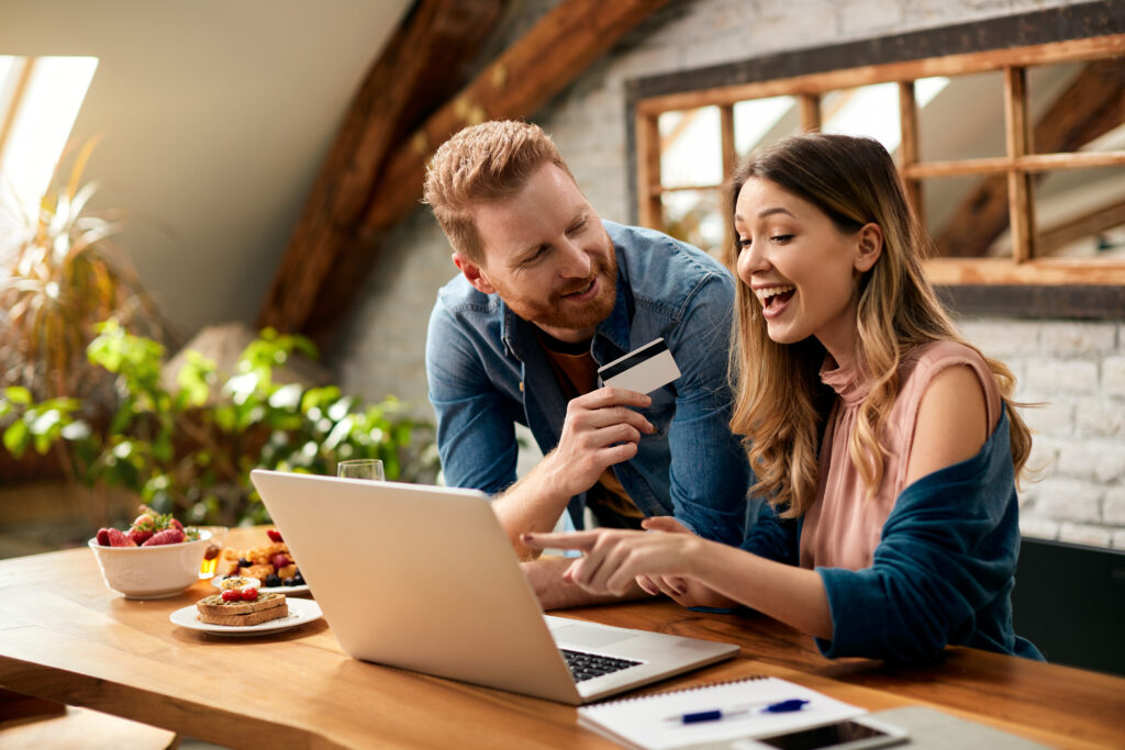 Excited woman pointing at a laptop next to a man handing her a credit card
