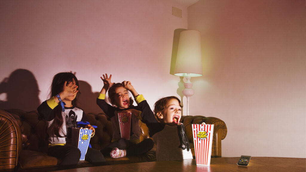 Three kids watching a movie with popcorn