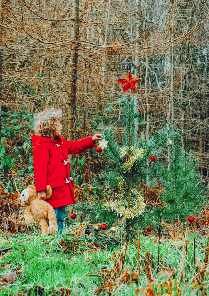Little boy decorating a Christmas tree in the woods