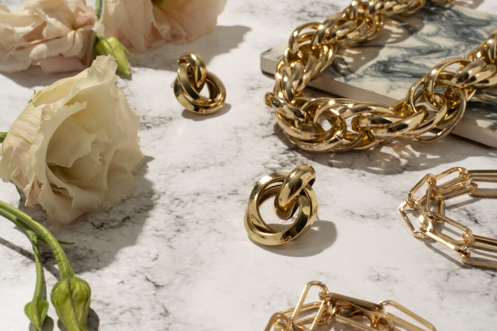 Chunky gold jewelry on a marble table with roses