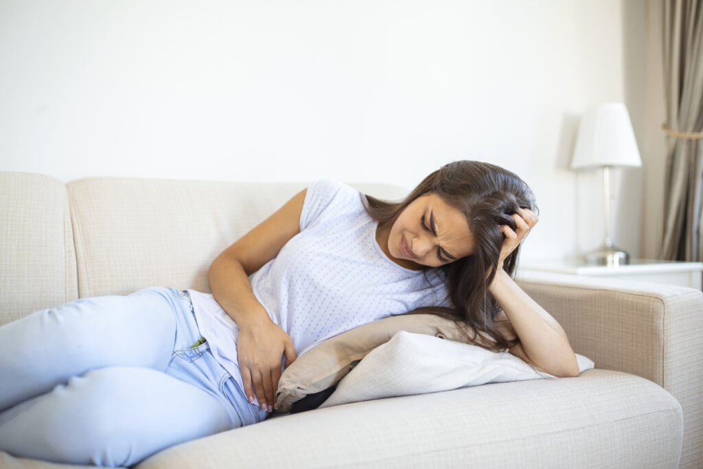Woman laying on sofa holding hands over her stomach in pain