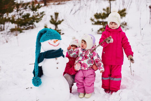 Kids in snow gear looking at a snowman