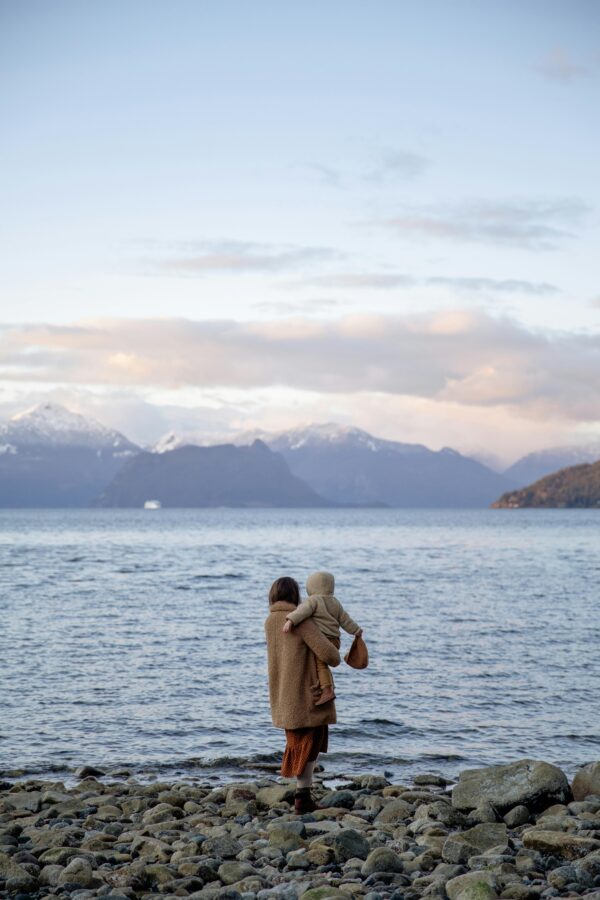 Mother and child standing by water with snowy mountains in the background