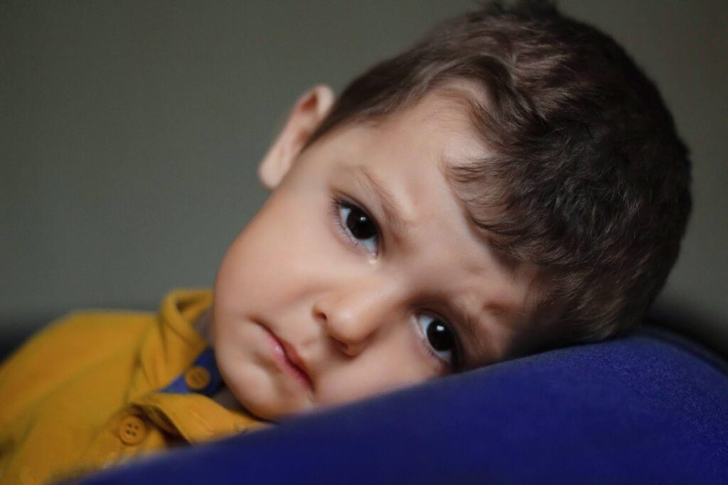 Young boy with brown eyes leaning on a parents shoulder