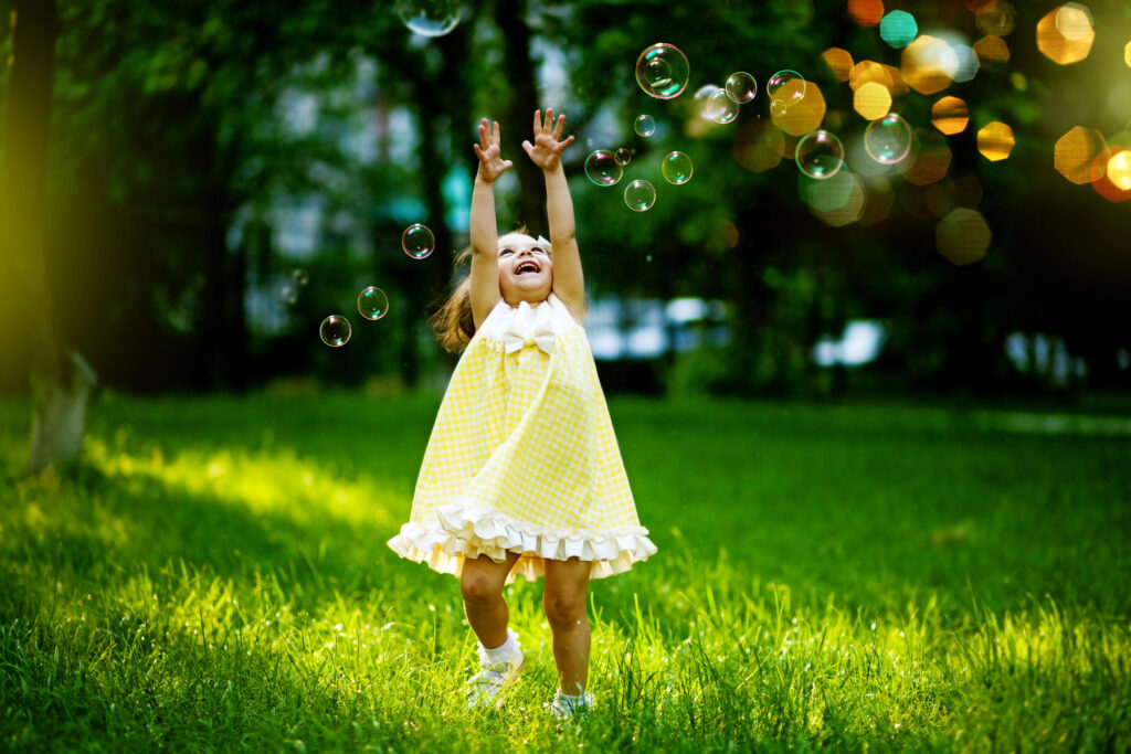 Little girl in a yellow dress catching bubbles in the garden