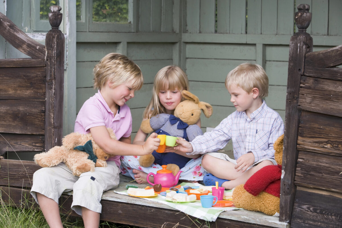 3 kids having a pretend tea party outdoors