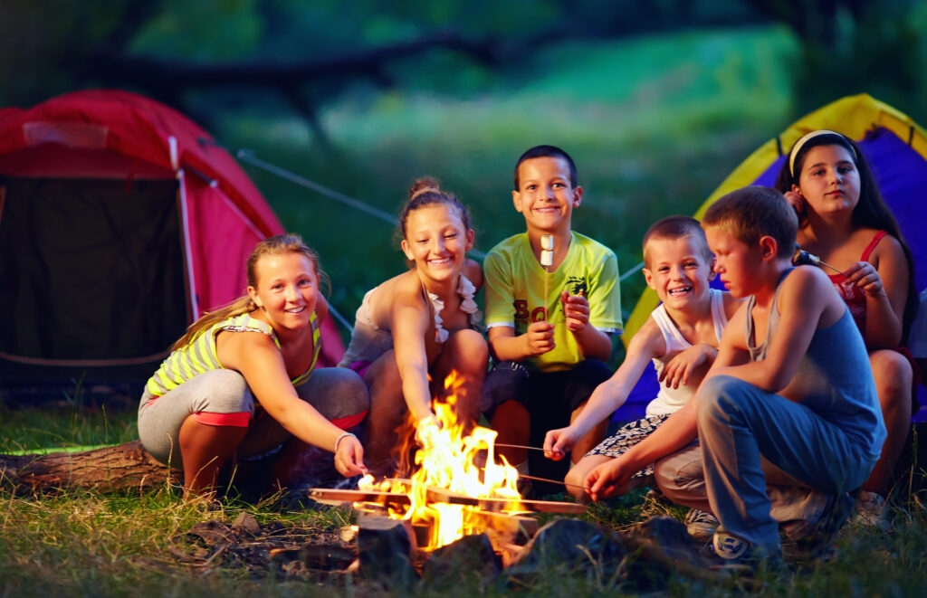 Kids at an outdoor camp roasting marshmallows on a camp fire