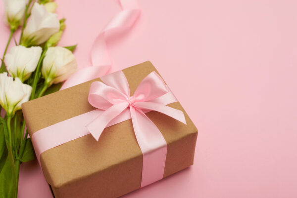 Wrapped gift with a pink bow on a pink background with white tulips on the side