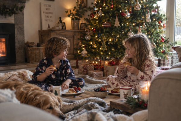 Two children having a picnic breakfast by a Christmas tree in a living room