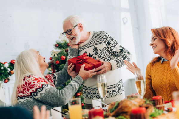 Smiling elderly gentleman gifting his wife a red gift-wrapped present